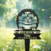 232-3 Black metal yard memorial sign with a smiling fluffy dog illustration, text “In Memory Of Tictoc” and dates “Nov 5 2018 - May 2024” staked in a sunlit meadow