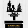 Black metal memorial sign showing a hunter silhouette walking with a rifle among pine trees, text "DAD" and dates "1946-2023" on a white wood background