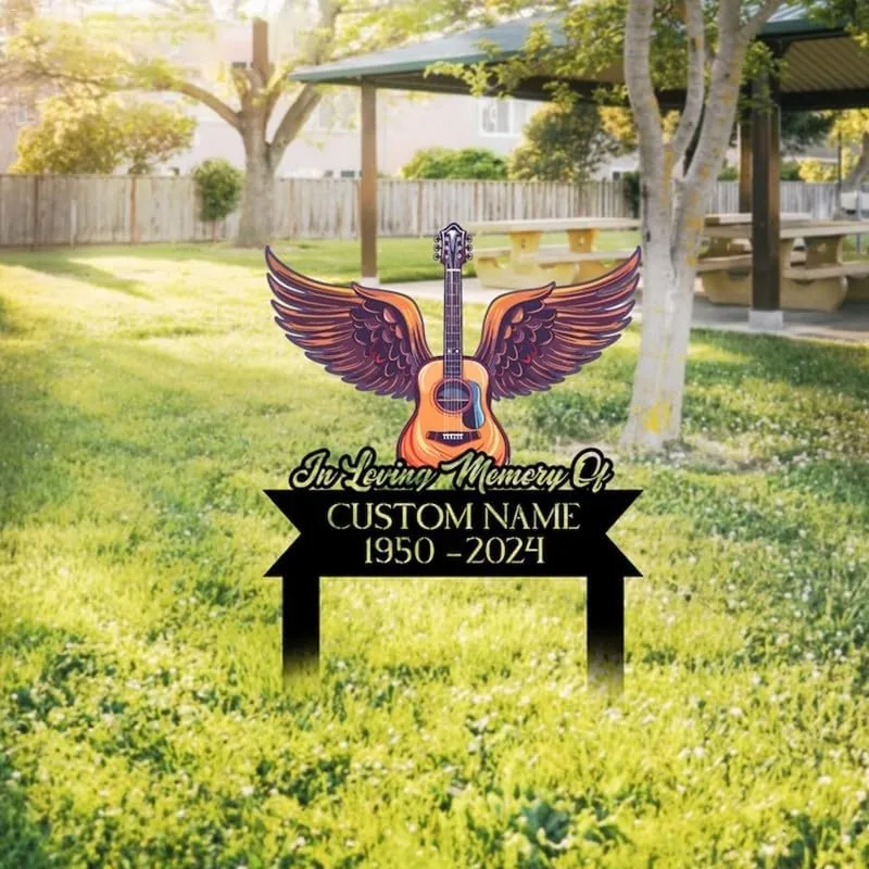 241-2 Outdoor memorial yard sign in grass showing a winged acoustic guitar and text "In Loving Memory Of" with placeholder "CUSTOM NAME 1950-2024" near a picnic shelter