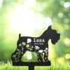 Black silhouette garden memorial stake in shape of a small dog with floral cutouts and text “Luna 2012-2024” against a sunlit green bokeh background