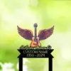 Memorial sign mockup with winged acoustic guitar graphic and text reading "In Loving Memory Of" and placeholder "CUSTOM NAME 1950-2024" on a soft green bokeh background