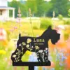 Black metal garden silhouette of a dog with floral cutouts and gold text reading “Luna 2012-2024” set against a blurred colorful wildflower field