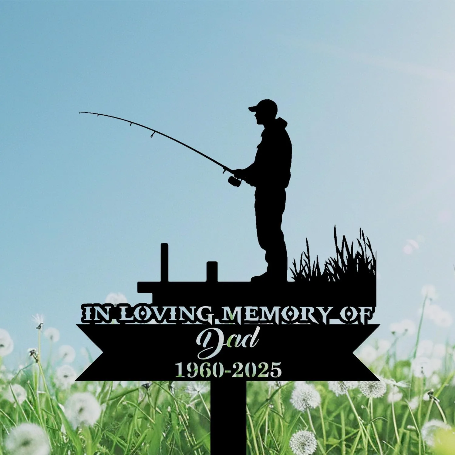 Silhouette memorial sign showing a man fishing on a dock above a banner reading "In Loving Memory of Dad 1960-2025" against a blue sky and dandelion field