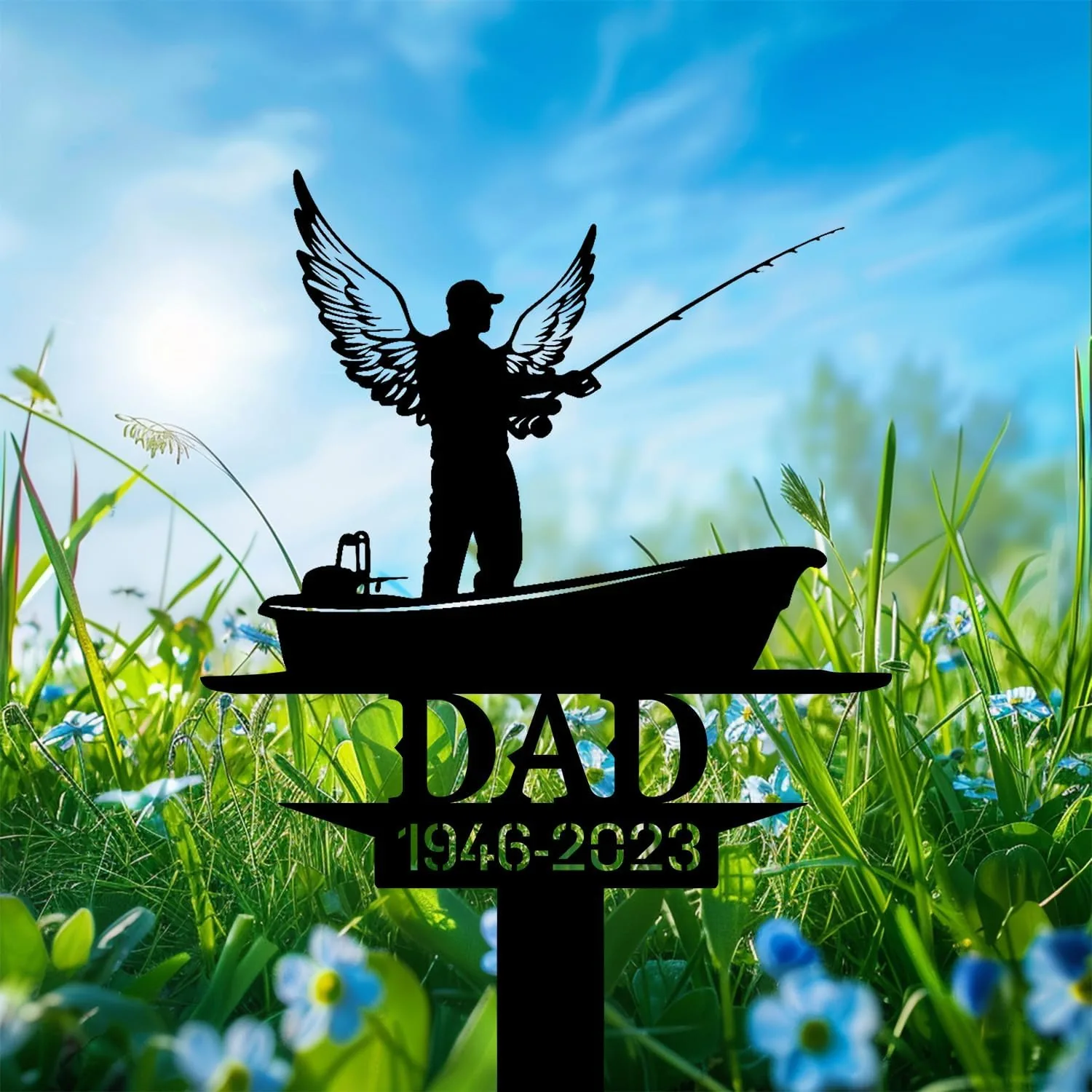 Black metal lawn memorial silhouette of an angelic fisherman in a boat with a fishing rod and the word DAD and dates 1946–2023 against a sunny grassy field with blue sky