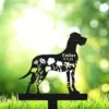 Black dog silhouette yard stake with floral cutouts and text "Ember 9.5.24" against a bright green bokeh background