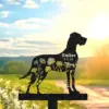 Black metal dog silhouette garden stake with floral cutouts and text "Ember 9.5.24" against a sunlit meadow background