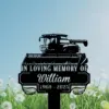 261 Black metal memorial sign in a grassy field featuring a combine harvester silhouette and text "In Loving Memory of William 1960 - 2025" against a blue sky
