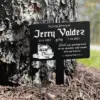 Black memorial stake beside a tree reading "In Loving Memory of Jerry Valdez 11-5-1952 7-26-2023" with a truck illustration and the inscription "Dad, your guiding hand on my shoulder will remain with me forever."