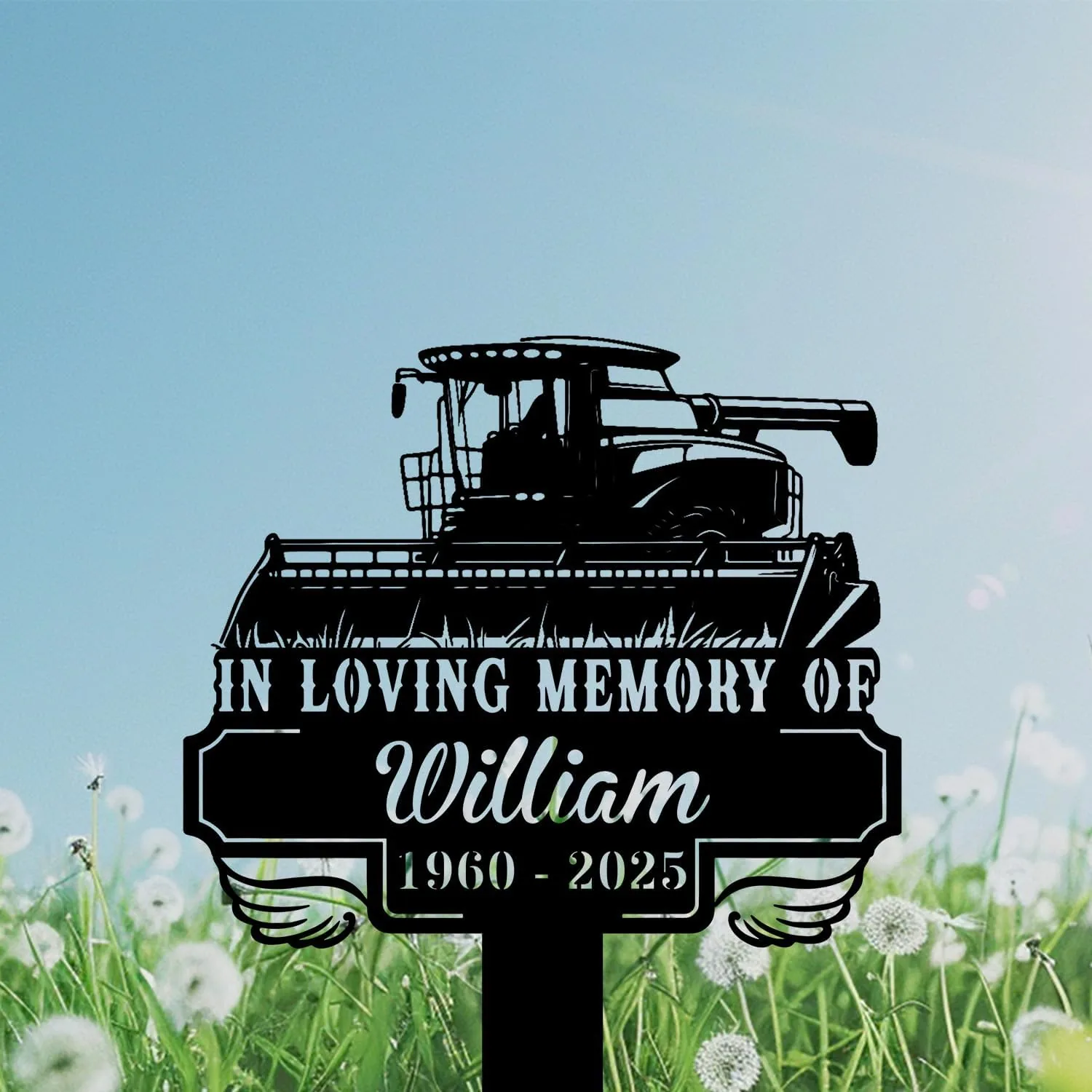 261 Black metal memorial sign in a grassy field featuring a combine harvester silhouette and text "In Loving Memory of William 1960 - 2025" against a blue sky