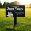 Black lawn memorial sign reading ‘In Loving Memory of Jerry Valdez 11-5-1952 7-26-2023’ with a truck illustration and the inscription ‘Dad, your guiding hand on my shoulder will remain with me forever,’ placed on grass outdoors