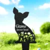 Black metal silhouette garden stake shaped like a small dog with cutout flowers and the text "Gizmo forever loved" displayed, placed in grassy lawn under a blue sky