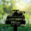 264 Black memorial sign with a combine harvester silhouette reading "In Loving Memory of William 1960 - 2025" placed in a sunlit daisy-filled green field