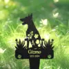 Black metal garden memorial stake shaped like a sitting dog with floral cutouts, engraved name "Gizmo" and dates "2012-2024" placed in green grassy yard