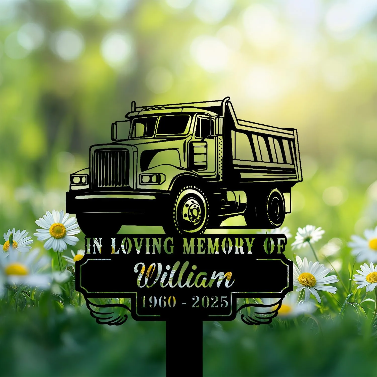 Black silhouette memorial sign shaped like a dump truck reading "In Loving Memory of William 1960 - 2025" placed among daisies in a sunlit green field