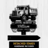 Black metal memorial sign showing a dump truck with text 'In Loving Memory of William 1960 - 2025' on a light wood background