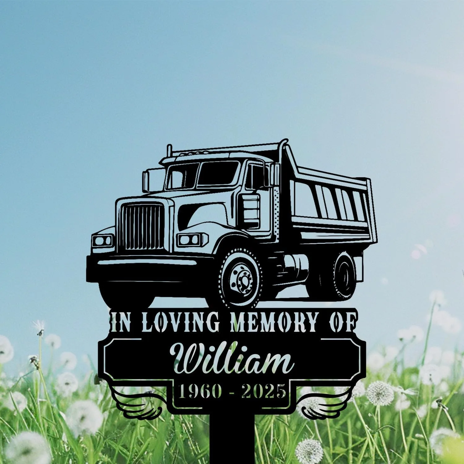 Black memorial sign with a dump truck illustration and text "In Loving Memory of William 1960 - 2025" set against a grassy field of dandelions and a blue sky