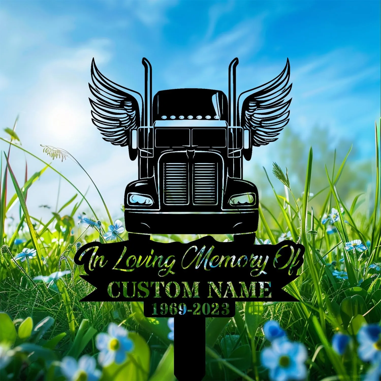 Black silhouette memorial sign of a winged semi truck reading "In Loving Memory Of" and "CUSTOM NAME 1969-2023" placed in a grassy field with blue sky and flowers