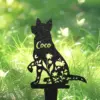 Black metal garden silhouette of a sitting dog with floral cutouts and the name "Coco" against a sunlit grassy background
