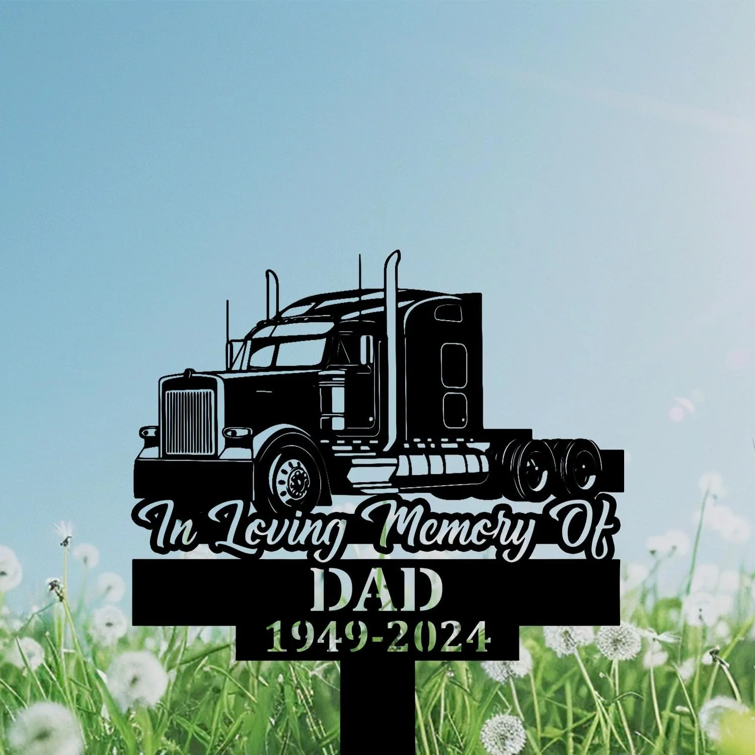 Black memorial yard sign showing a semi truck silhouette with script text "In Loving Memory Of" and block text "DAD 1949-2024" against a grassy dandelion field and blue sky