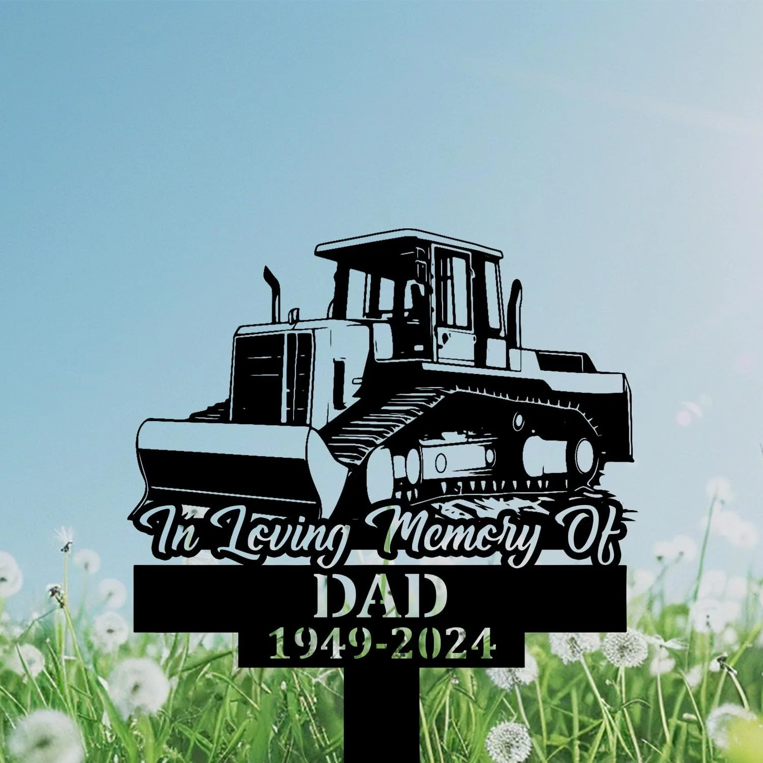 303 Black memorial lawn sign showing a bulldozer illustration and text "In Loving Memory Of DAD 1949-2024" against a blue sky and dandelion field