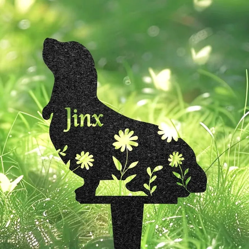 Black metal dog-shaped garden stake with floral cutouts and the name "Jinx" against green grass background