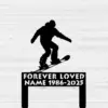Black silhouette of a snowboarder jumping above a memorial plaque reading "FOREVER LOVED NAME 1986-2025" on a light wood plank background