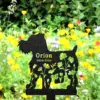 Black metal garden memorial silhouette of a small dog with cutout flowers and text "Orion 2010-2024" staked in a colorful wildflower meadow