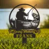 Black metal memorial stake showing a fisherman in a boat catching a fish with the text "In Loving Memory Of FRANK" placed in grass by a lakeshore at sunset