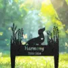 Black metal garden memorial stake with a dachshund silhouette, plant cutouts, the name "Harmony" and years "2006-2024" against a sunlit grassy background