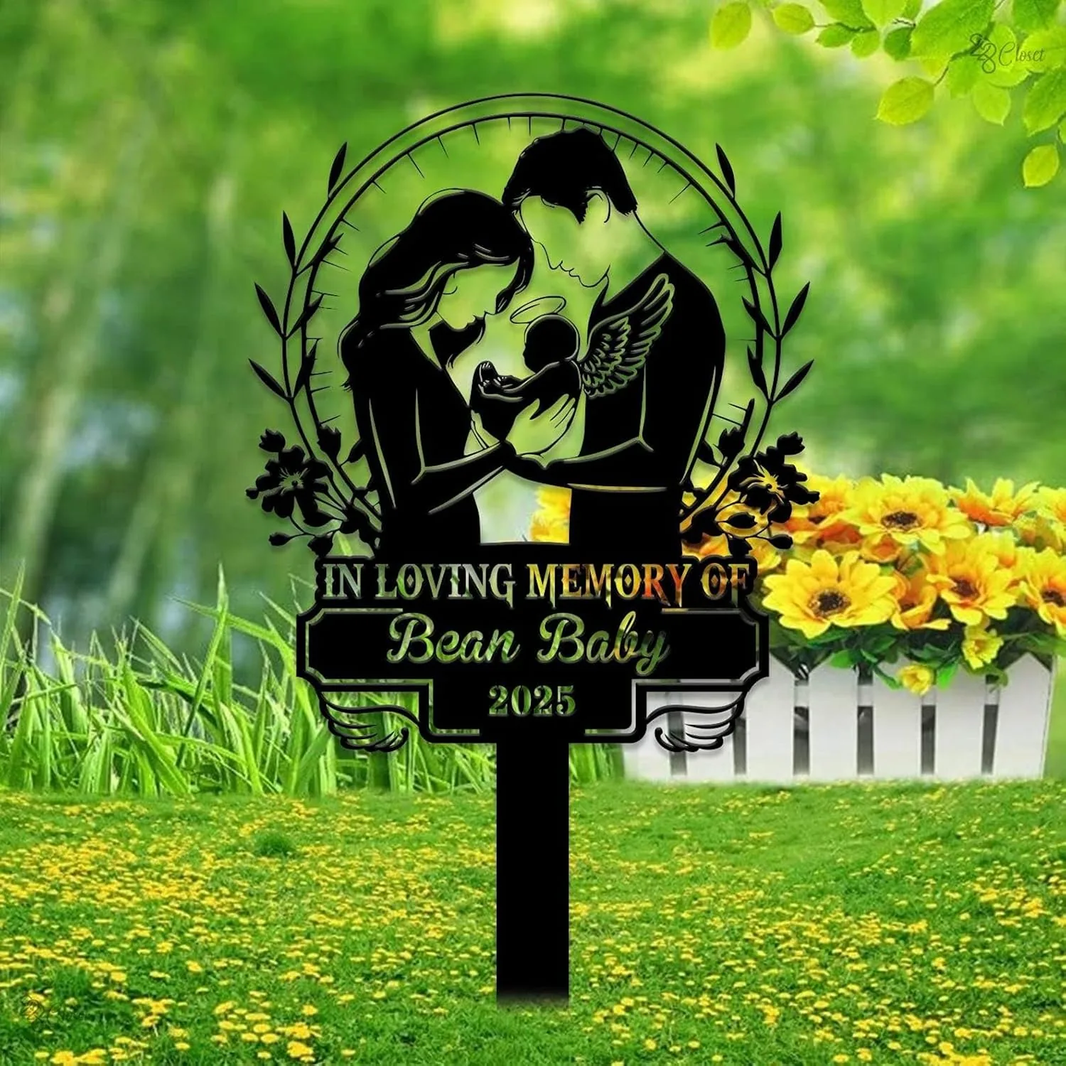 342 Black memorial garden sign showing a mother and father holding an angel baby with text "In Loving Memory of Bean Baby 2025" placed in a grassy yard with yellow flowers and a white picket fence planter