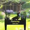 Black metal garden memorial stake shaped like a dachshund with floral cutouts, engraved 'Harmony 2006-2024', placed in a lush backyard lawn with flowers and a wooden garden shed