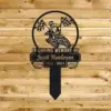 353 Black metal memorial stake reading "In Loving Memory of Jacob Henderson 1956 - 2024" with a motocross rider and checkered flags mounted on a wooden plank background