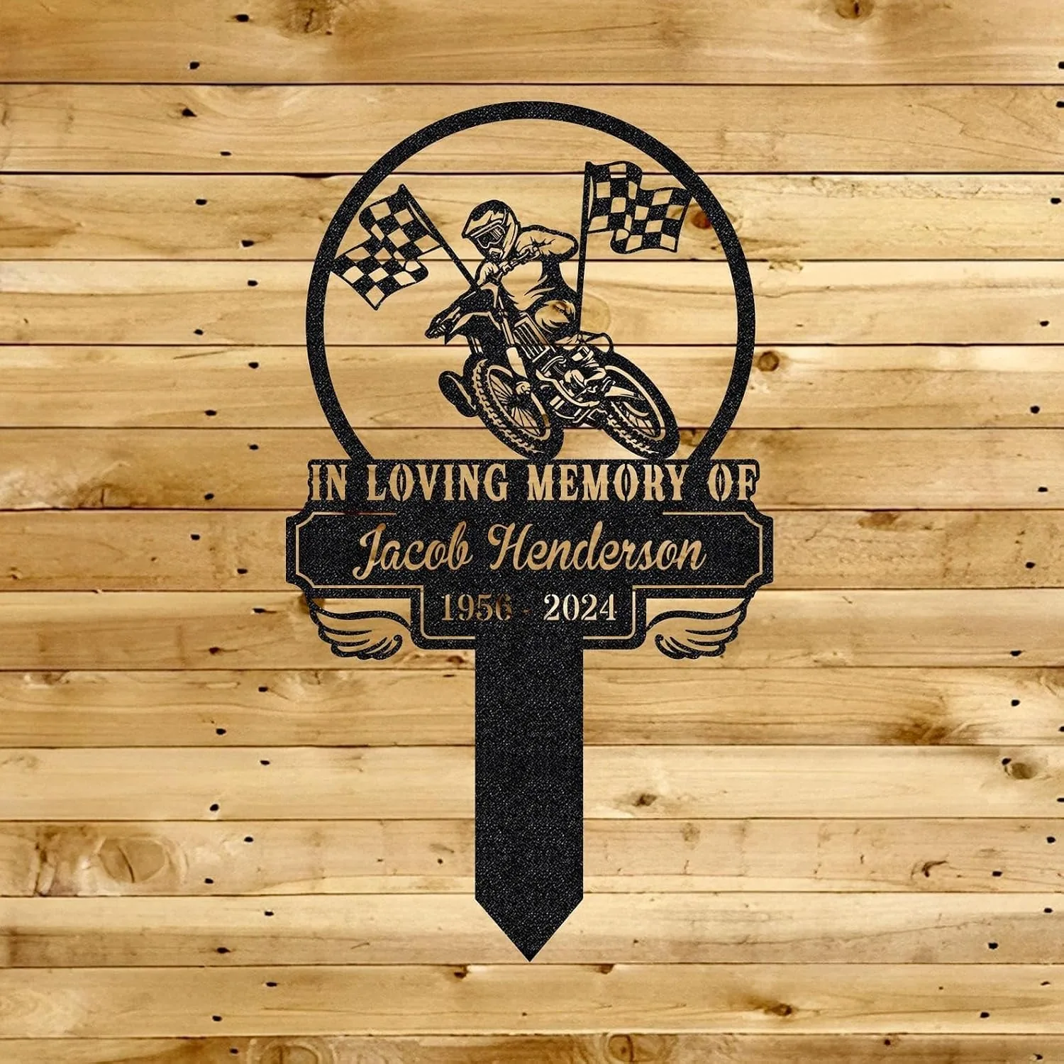 353 Black metal memorial stake reading "In Loving Memory of Jacob Henderson 1956 - 2024" with a motocross rider and checkered flags mounted on a wooden plank background
