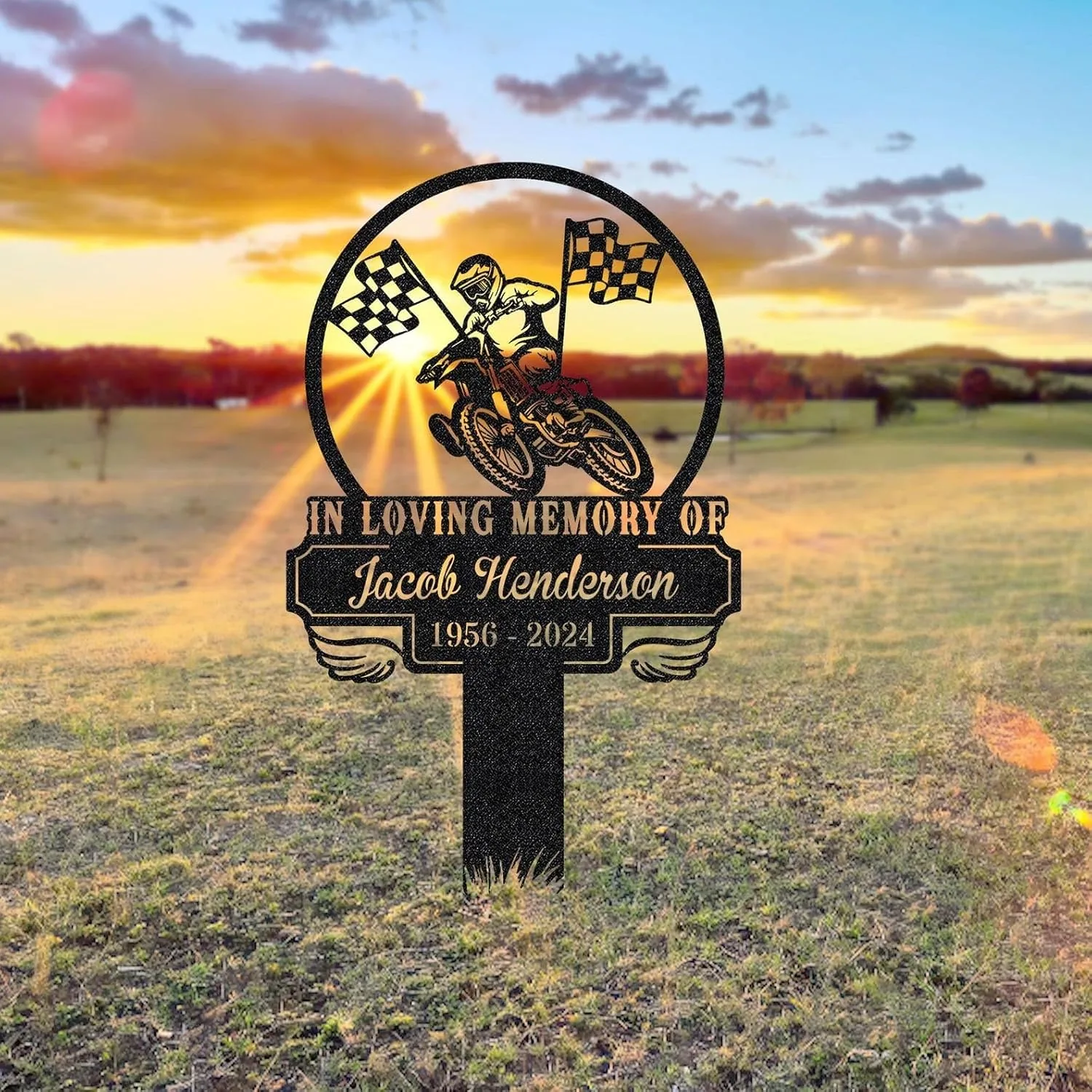 354 Memorial metal sign in a field at sunset reading “In Loving Memory of Jacob Henderson 1956 - 2024” with a motocross rider and checkered flags inside a circular frame