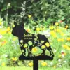 Black French bulldog grave marker silhouette with floral cutouts reading "Sable 2010-2024" placed in a flower-filled garden