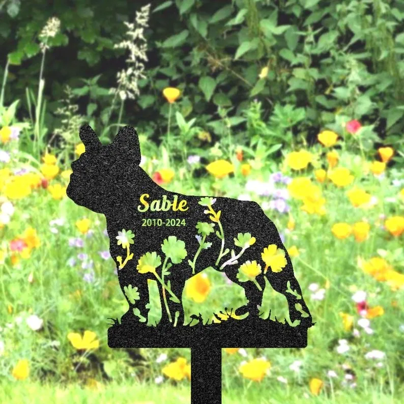 Black French bulldog grave marker silhouette with floral cutouts reading "Sable 2010-2024" placed in a flower-filled garden