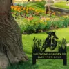 Black metal memorial lawn sign with a motocross rider silhouette and text “IN LOVING MEMORY OF JACK 1987-2024” placed on grass near a tree and colorful flowerbeds