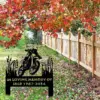 Autumn yard with red and orange tree leaves, a wooden picket fence, fallen leaves on grass, and a black metal memorial sign reading "IN LOVING MEMORY OF JACK 1987-2024" with a motorcycle silhouette.