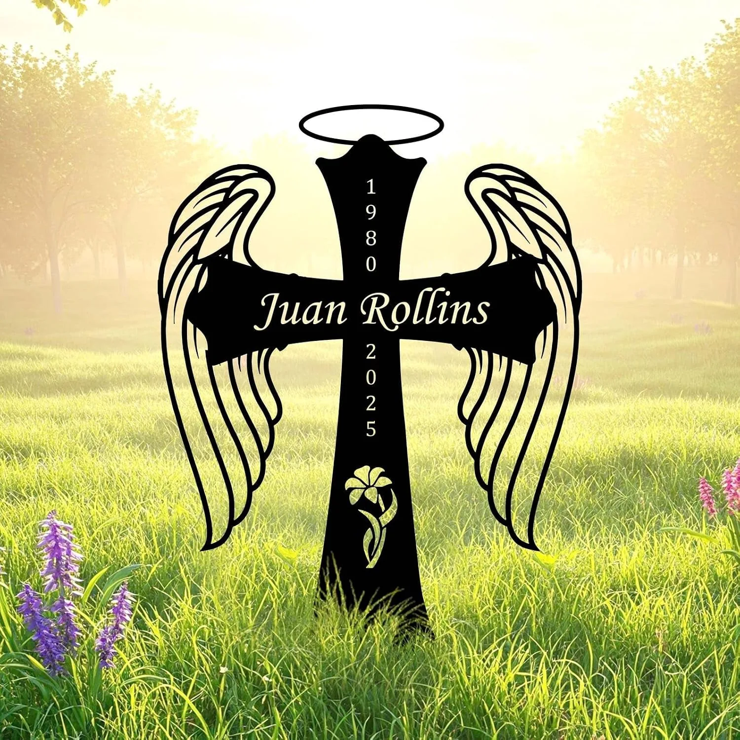 Black angel wing cross garden stake with halo reading "Juan Rollins" and dates 1980–2025 set in a sunlit grassy field with purple flowers