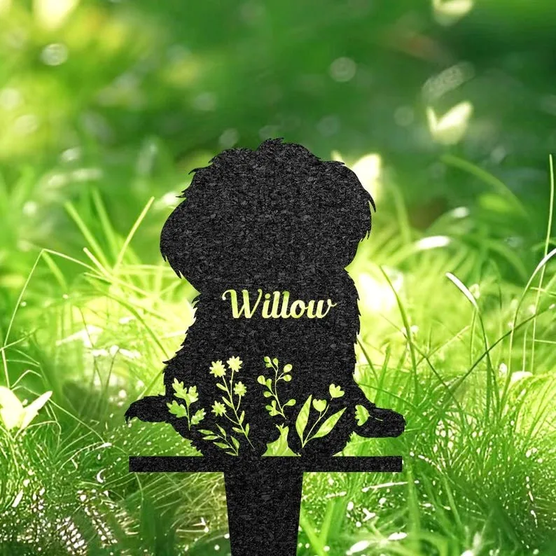 Black metal silhouette garden stake of a sitting dog with floral cutouts and the name 'Willow' against sunlit green grass