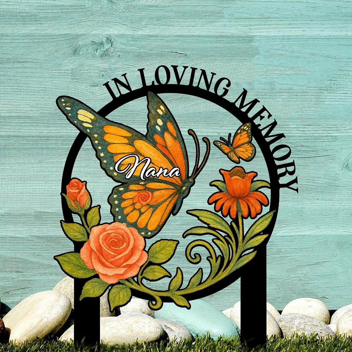 Outdoor memorial sign with painted orange monarch butterfly, roses and flowers on a turquoise wood background, text reads "In Loving Memory" and "Nana"