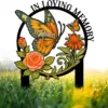 Memorial garden stake with a large orange and green butterfly, flowers and roses, text “In Loving Memory” and name “Nana” against dewy grass background
