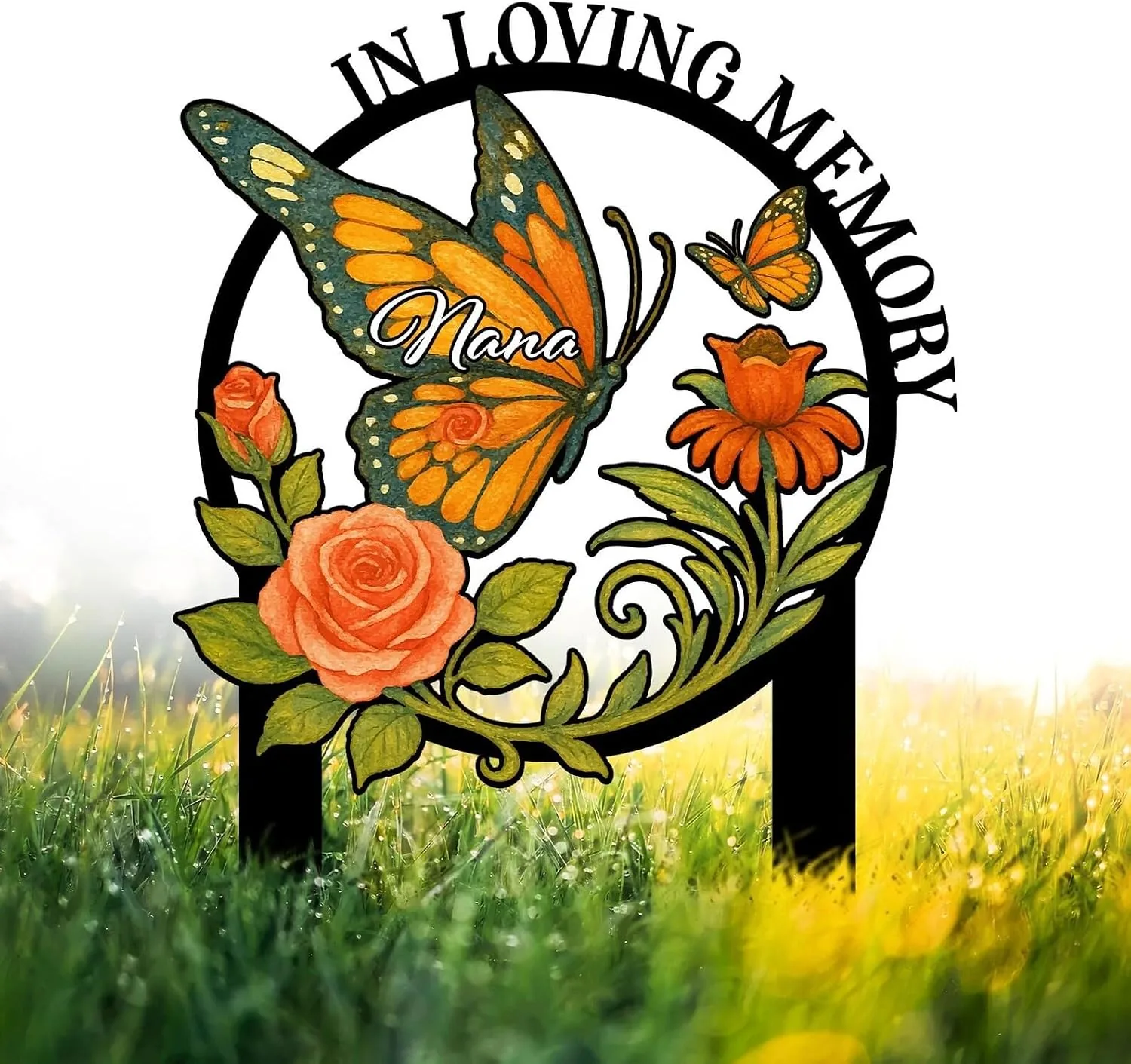 Memorial garden stake with a large orange and green butterfly, flowers and roses, text “In Loving Memory” and name “Nana” against dewy grass background