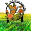 Black circular memorial garden stake with orange butterfly labeled "Nana", roses and flowers set in bright green grass