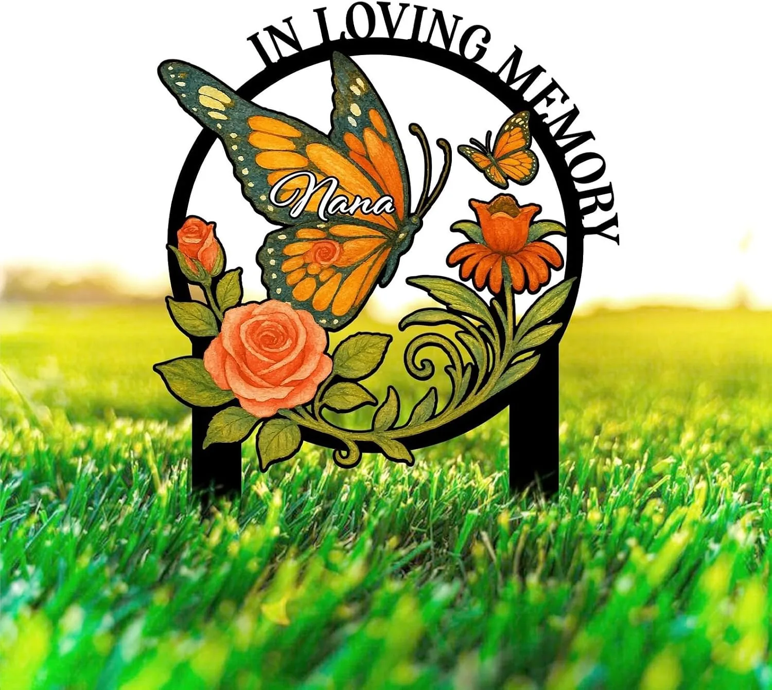 Black circular memorial garden stake with orange butterfly labeled "Nana", roses and flowers set in bright green grass