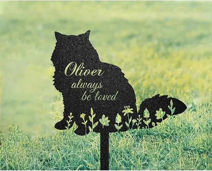 Black metal cat-shaped garden sign on a stake in grass reading "Oliver always be loved" with cutout floral details