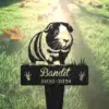 Black metal memorial stake with a guinea pig illustration and the name "Bandit" above dates "2020-2024" placed in sunlit grass