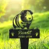 Black silhouette garden memorial stake of a guinea pig above text "Bandit" and years "2020-2024" set in sunlit green grass