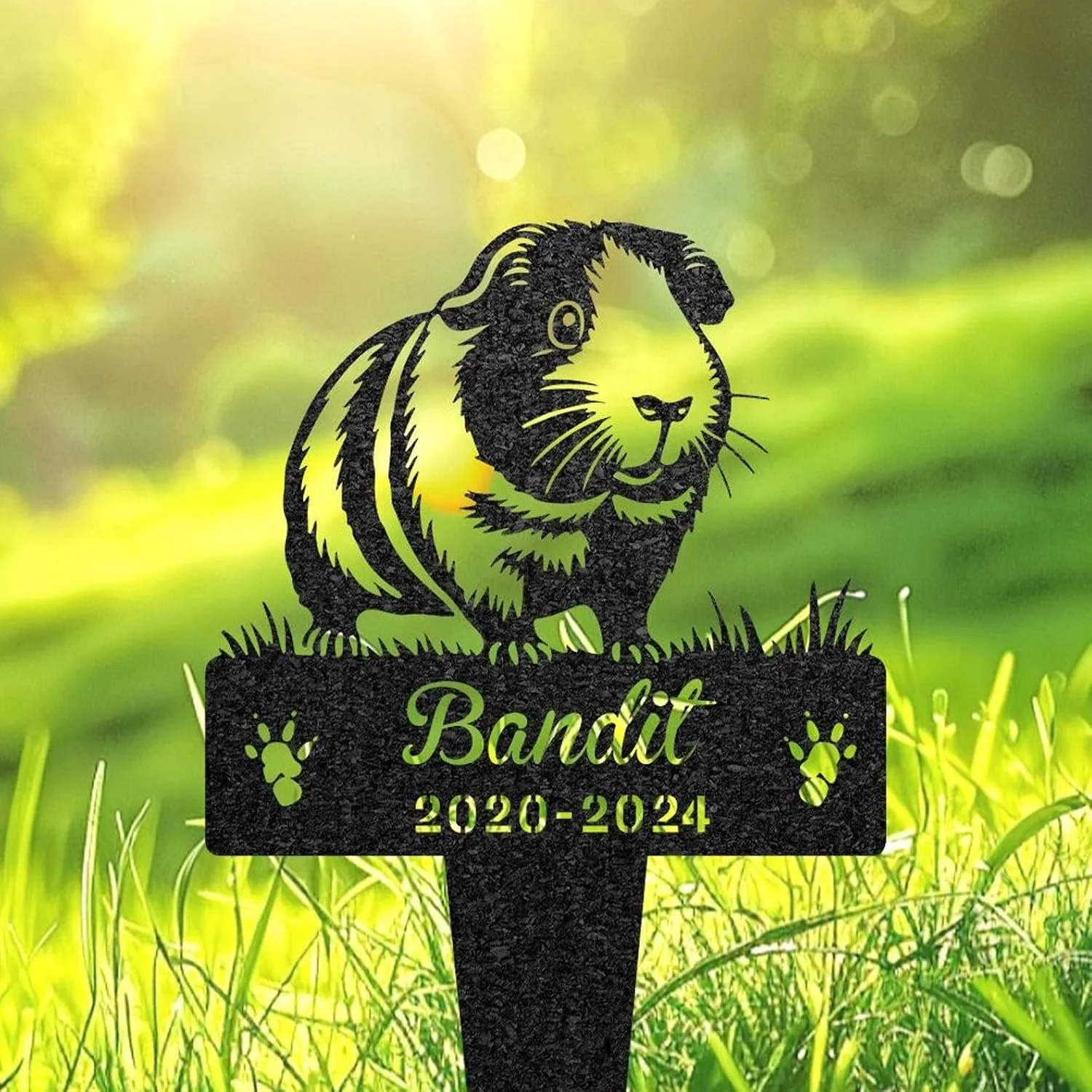 Black silhouette garden memorial stake of a guinea pig above text "Bandit" and years "2020-2024" set in sunlit green grass