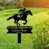 Black metal memorial yard sign showing a jockey on a horse above text 'In Loving Memory of Custom Name 1940-2025' placed on a sunny green lawn near flowering shrubs